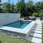 Small raised backyard pool with stone patio