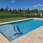 Rectangular backyard swimming pool with stone deck.